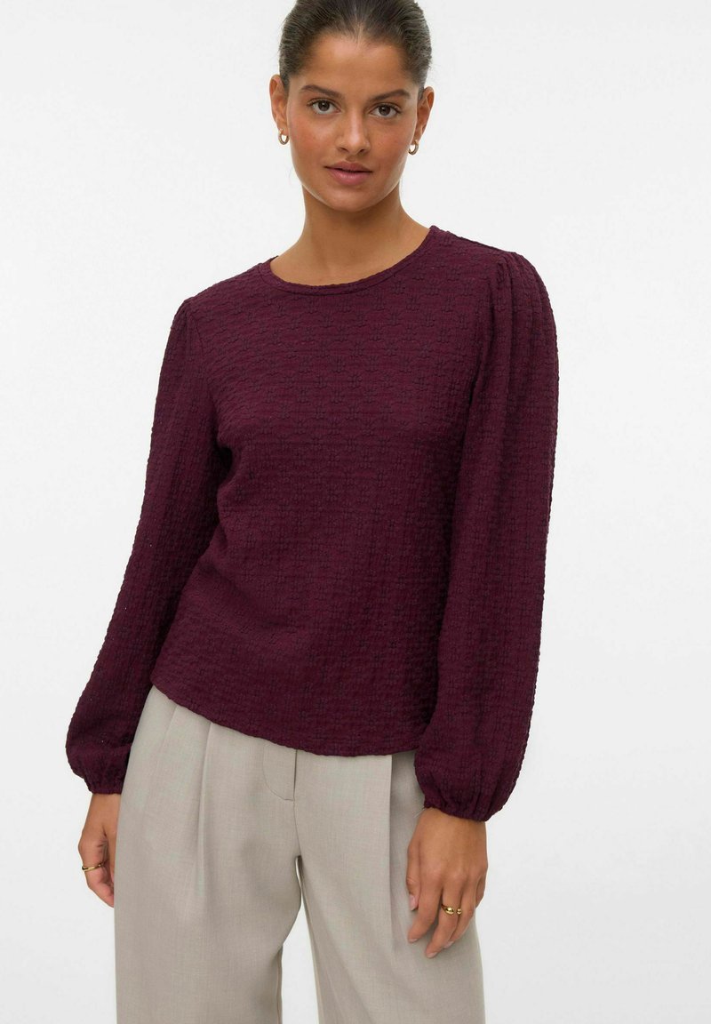 Bordeaux gekleurde blouse met textuur, lange mouwen, een ronde hals en gathered manchetten, gecombineerd met lichtgrijze op maat gemaakte broek.