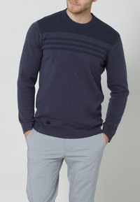 Navy blue sweater with a textured shoulder, horizontal stripes across the chest, and ribbed cuffs and hem. Soft, knitted fabric.
