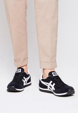 Black and white athletic sneakers with suede and mesh materials, featuring a rounded toe, white side stripes, and textured rubber soles.