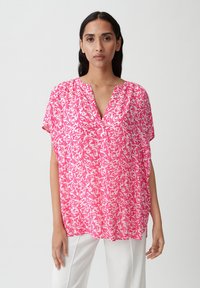 Blusa a fiori rosa con scollatura a V, maniche corte e vestibilità rilassata. Realizzata in tessuto leggero, presenta una morbida consistenza e un drappeggio fluido.