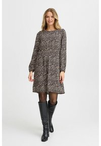 Braun gemustertes Kleid mit langen Ärmeln, lockerer Passform und ausgestelltem Saum. Kombiniert mit schwarzen kniehohen Stiefeln und transparenten schwarzen Strumpfhosen.