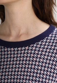 Pull en maille présentant un motif pied-de-poule en marine, rose clair et gris. Encolure ronde large en côtes, texture douce et tissu de poids moyen.