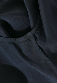 Gros plan d'un tissu noir montrant des coutures détaillées et des plis dans le matériau.