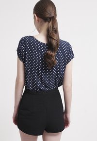 Marineblaue Bluse mit Polka-Dots und kurzen Ärmeln, kombiniert mit schwarzen, hochgelegten Shorts. Glattes Material mit einem strukturierten Taillenbund.
