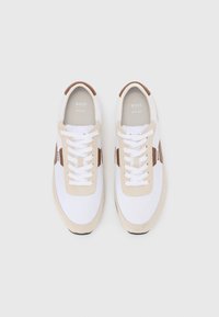 Hvite sneakers med beige semsket huddetaljer, med rund tå, flate lisser og strukturert såle. Logo trykket på tungen og siden.