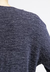 Mörkblå stickad tröja med en texturerad yta och vid rundhalsning, som visar ett subtilt varierat garnmönster.