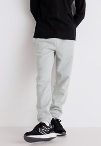 Grijze sweats met een zachte katoen met een tapered fit en elastische boorden, gecombineerd met zwarte sportschoenen met witte accenten.
