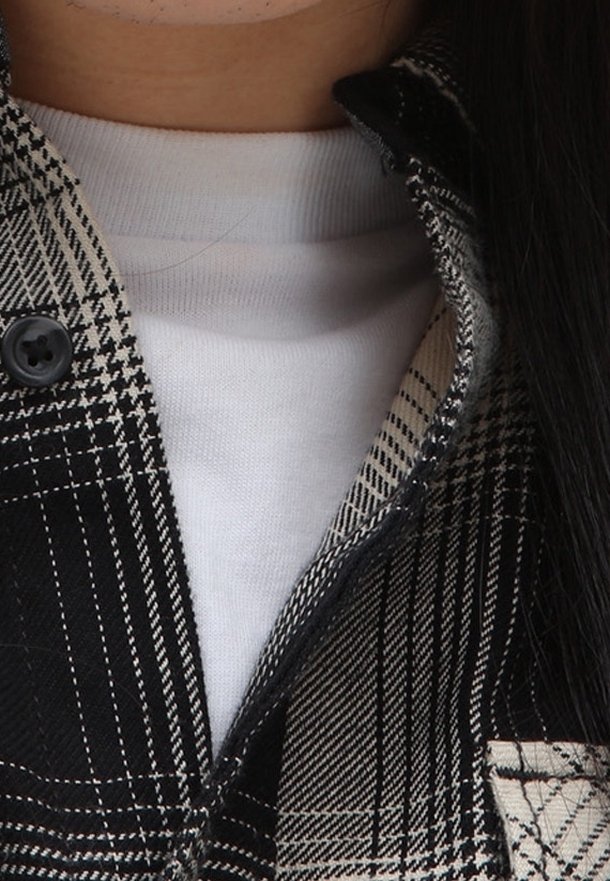 Gros plan d'une personne portant une veste à carreaux noire et blanche par-dessus un t-shirt blanc à col rond, avec de longs cheveux foncés visibles sur le côté droit.