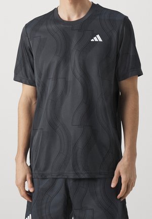 Mann trägt schwarzes Adidas-Sport-T-Shirt und Shorts mit abstrakten wellenförmigen Linienmustern und weißem Adidas-Logo auf Brust und Bein.