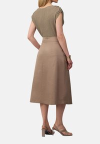 Strickoberteil mit umgeschlagenen Ärmeln, kombiniert mit einem beigen Midikleid. Das Outfit besticht durch weiche Texturen und eine taillierte Silhouette. Die Schuhe sind nacktfarbene, offene High Heels.