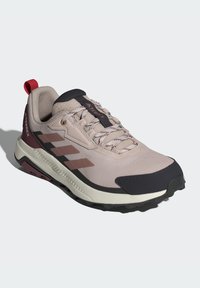 Light pink trail running shoe with textured features, dark navy accents, and a lugged sole. Includes black laces and a red pull tab.