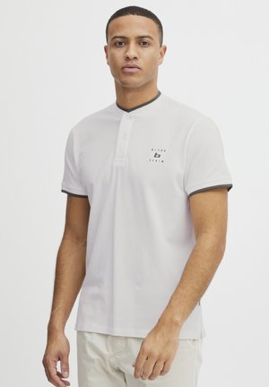 Polo blanc à manches courtes avec col, bordure sombre contrastante et petit logo sur la poitrine gauche. Fabriqué en tissu en coton lisse.