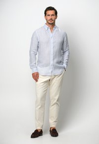 Jasnoniebieska i biała w paski koszula z długimi rękawami i kołnierzykiem zapinanym na guziki, noszona z kremowymi spodniami i brązowymi zamszowymi mokasynami.