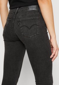Fekete farmernadrág, slim fit szabással, két tónusú varrással, jellegzetes hátsó zsebekkel és b�őrből készült márkajelzéssel a derékpánton.