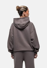 Felpa grigia oversize con cappuccio, realizzata in tessuto morbido. Presenta spalle scese e polsini a coste per una vestibilità rilassata.