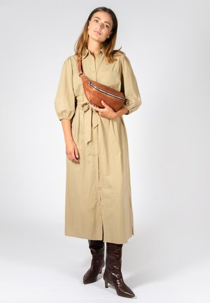 Abito beige con bottoni a camicia e vita con cintura, maniche lunghe a palloncino, abbinato a stivali marroni al ginocchio in stampa coccodrillo e una borsa a tracolla marrone.