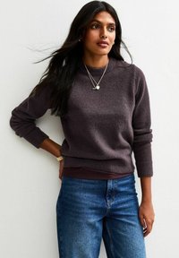 Donkerpaarse trui van zachte stof, met een ronde hals en ribbelmanchetten, gecombineerd met blauwe jeans voor een casual look.