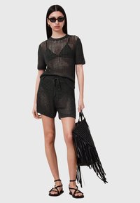Sort strikket to-delt outfit bestående af en kortærmet, løs-fittet top og shorts. Det teksturerede materiale har et åbent vævdesign. Tilbehøret inkluderer en stor sort vævet taske med frynser.