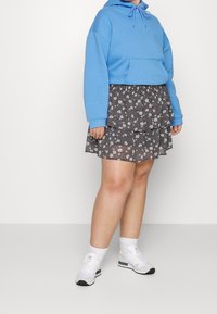 Vaaleansininen huppu-sweatshirt, jossa on etutasku, yhdistettynä korkea vyötäröiseen, kerrokselliseen mustaan hameeseen, jossa on valkoinen kukkakuosi. Valkoiset lenkkarit.