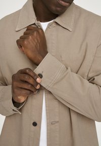 Helles beigefarbenes Jackett aus strukturiertem Stoff, mit klassischem Kragen, geknöpften Manschetten und Knöpfen vorne. Sieht lässig und funktional aus.