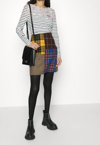 Gestreiftes Langarmoberteil mit pinken Akzenten, kombiniert mit einem Patchwork-Minirock, der verschiedene Karomuster in Gelb, Braun und Blau zeigt. Schwarze Chelsea-Stiefel.