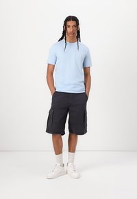 Ανοιχτό μπλε μπλουζάκι crew-neck, σκούρες cargo βερμούδες με πλαϊνές τσέπες, λευκά αθλητικά παπούτσια και κάλτσες έως τον αστράγαλο. Καθαρή, casual εμφάνιση.