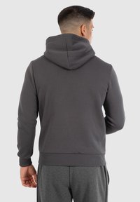 Sweat à capuche gris foncé, fabriqué en tissu doux. Présente un ourlet et des poignets côtelés, avec une capuche proéminente et un design arrière épuré.