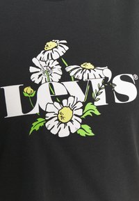 Černé bavlněné tričko s bílou květinovou grafikou se žlutými středy a zelenými listy, vedle loga "LEVI'S" v tučném bílém písmu.