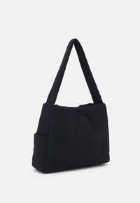 Sac à épaule noir matelassé avec une forme triangulaire plate, texture rembourrée et une seule sangle large. Comprend une poche latérale pour un espace de rangement supplémentaire.