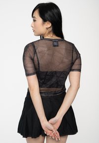 Black mesh top with short sleeves, featuring a geometric pattern and textured design. Paired with a flared black skirt, showcasing a simple silhouette.