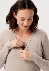 Beige ribbelshirt met lange mouwen en een V-hals, voorzien van een geplooid midden en een subtiele opening. Zachte textuur, aansluitende mouwen.