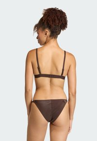 Brązowy bikini w prążki, z cienkimi regulowanymi ramiączkami i trójkątnym fasonem dolnej części. Gładka tekstura z detalem logo na pasku.