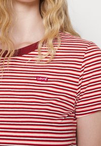 Blondyn w czerwono-biało-burgundowej koszulce w paski marki Levi's, z falującymi włosami widocznymi na ramieniu.