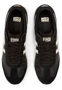 Black athletic shoes with a fabric and suede upper, featuring white stripes, black laces, and a rubber sole. Onitsuka Tiger logo visible.