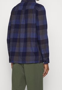 Niebieska i szara koszula w kratę z długim rękawem, z kołnierzykiem i zaokrąglonym dołem. Wykonana z teksturowanej tkaniny.