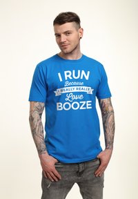 Blå bomulds T-shirt med hvid tekst: "JEG LØBER fordi jeg virkelig, virkelig elsker ØL." Korte ærmer og rund halsudskæring.