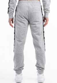 Graue Jogginghosen aus weichem Material, mit schwarzem Seitentape mit Branding, elastischem Bund und gerippten Bündchen für einen bequemen Sitz.