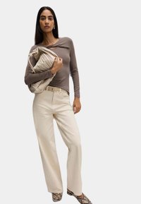 Bruine langemouwen top met een twistdetail, crèmekleurige wijde broek en een beige geplooide handtas. Textuur met slangenprint schoenen maken de look compleet.