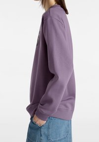 Sudadera morada con cuello redondo, puños y dobladillo acanalados. Presenta un gran gráfico en la parte delantera y una textura de tela suave.