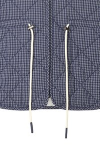 Modrá prešívaná bunda s bielym mriežkovým vzorom, so stredným zipsom, dvoma vreckami a bielymi šnúrkami s kovovými koncovkami.