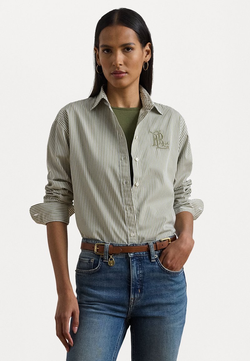 Zöld és fehér csíkos ing, mellkason logóval, zöld alsó résszel, kék farmernadrággal és barna övvel párosítva.