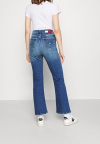 Vaqueros acampanados de talle alto en denim azul medio con un leve desgaste, que cuentan con dos bolsillos traseros y una etiqueta de marca en la cintura.