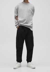 Szary sweatshirt z okrągłym dekoltem i małym białym logo, w połączeniu z czarnymi spodniami cargo z bocznymi kieszeniami oraz białymi sneakersami.