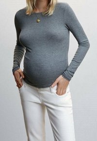 Top de manga larga de rayas grises combinado con pantalones blancos. El top es ajustado, resaltando una barriga redondeada. Destaca un collar de péndulo dorado.