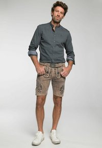 Shorts de lederhosen marrones con bordados florales, combinados con una camisa azul con estampado y zapatillas blancas. Presenta botones en el frente y cinturón.