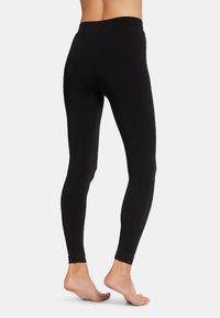 Zwarte legging gemaakt van rekbaar materiaal, met een hoge tailleband en een gladde textuur, die taps toeloopt naar enkelhoogte zonder zichtbare naden.
