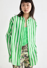 Grønn og hvit stripete oversized skjorte med "sports" trykket. Kombinert med en grønn tank top og mønstrede leggings med blomster- og dyremotiver.