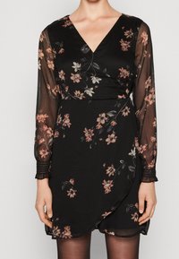 Vestido negro envolvente con patrón floral en rosa y blanco. Presenta mangas largas translúcidas y escote en V. Tejido suave, puños fruncidos.