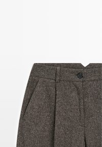 Pantaloni in tweed marrone con pince frontali, tasche laterali, passanti per cintura e chiusura con bottone nero su sfondo bianco.
