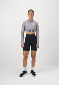 Lys grå, kort athletic topp med glidelås krage, kombinert med høyt liv sorte shorts. Sorte logo detaljer på toppen og shortsene. Sorte joggesko.